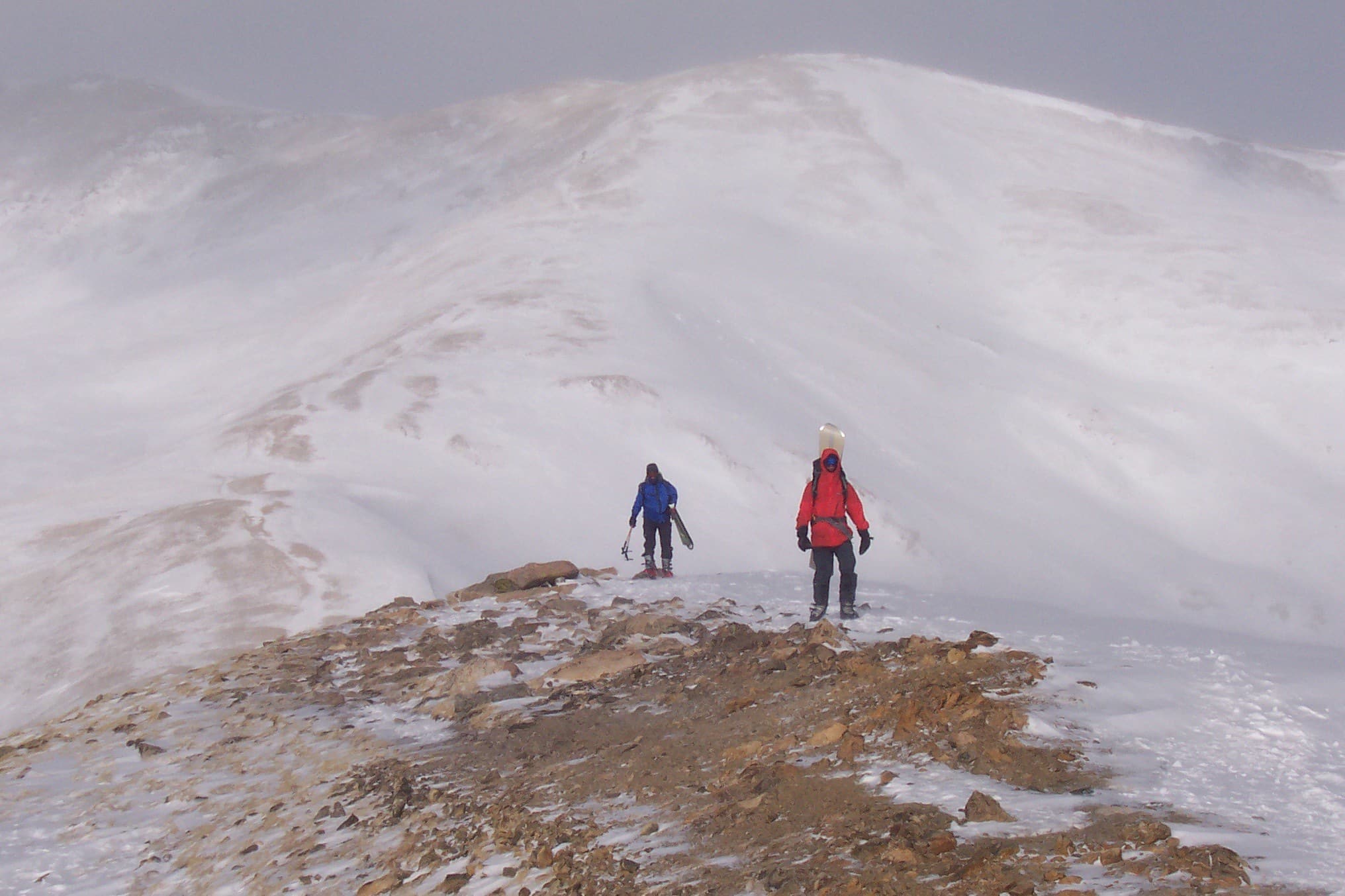 Two people walking with snowboards on their backs along a mountain ridge on Loveland Pass