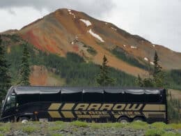 Black Arrow Stage Lines coach bus parked in front of a mountain with fall colors