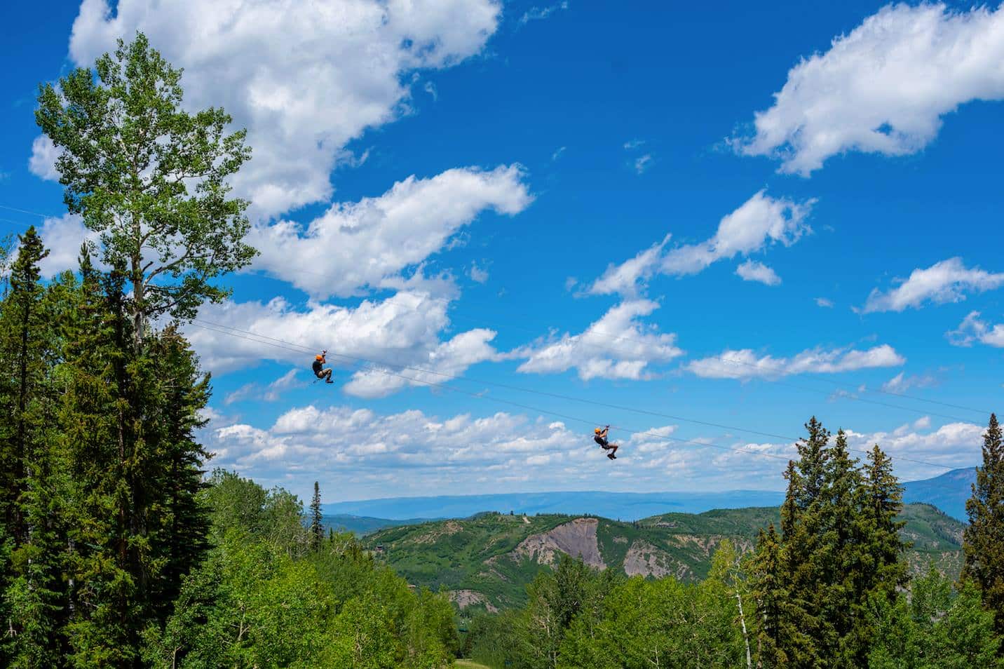 Two people ziplining high above mountain forest