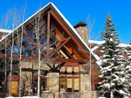 Front entrance to Bear Creek Lodge, a wooden A-frame building with several snow covered trees lining the entryway