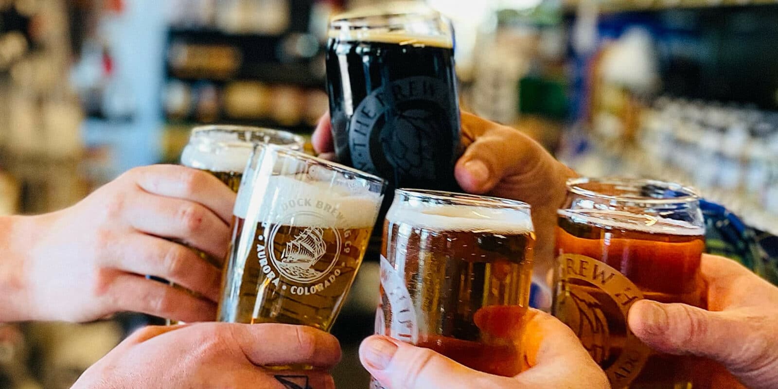 Five hands holding homebrew glasses of beer and toasting at The Brew Hut