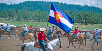 Cowboy holding a Colorado state flag at a rodeo in Pagosa Springs