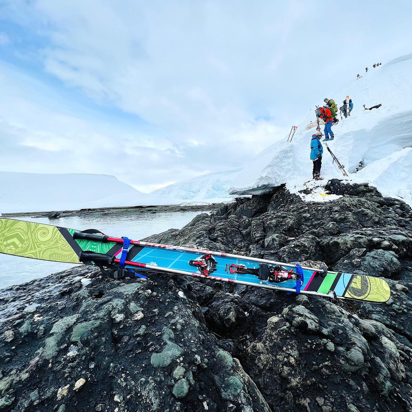 Colorful Folsom ski sitting on a rock in front of climbers in Antarctica.