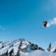 Skier in a red jacket on Icelantic Skis sending it off a huge jump on a bluebird skies day