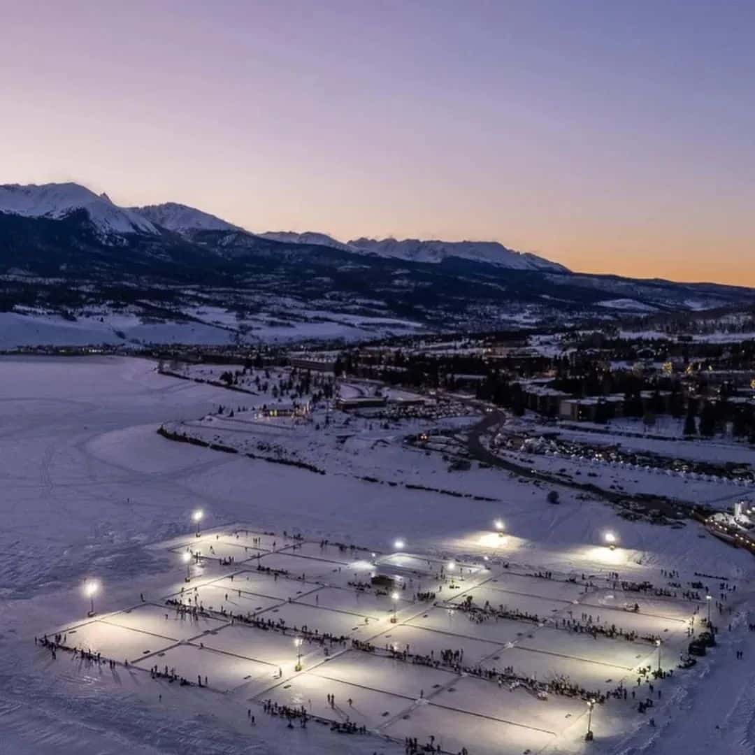 Several lighted ice rinks on a pond with mountains and a sunset in the background