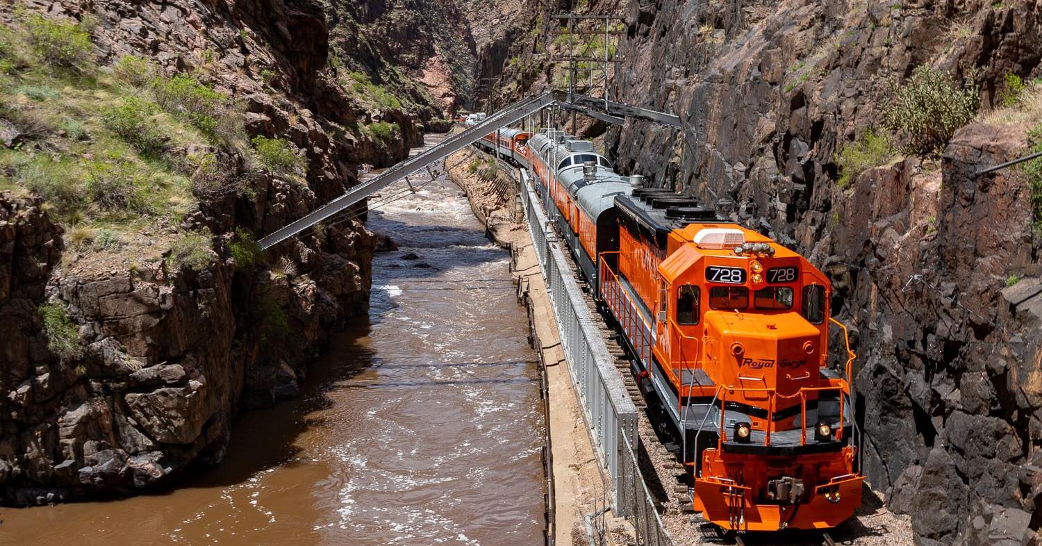 Bright orange train on trestles in canyon next to a river