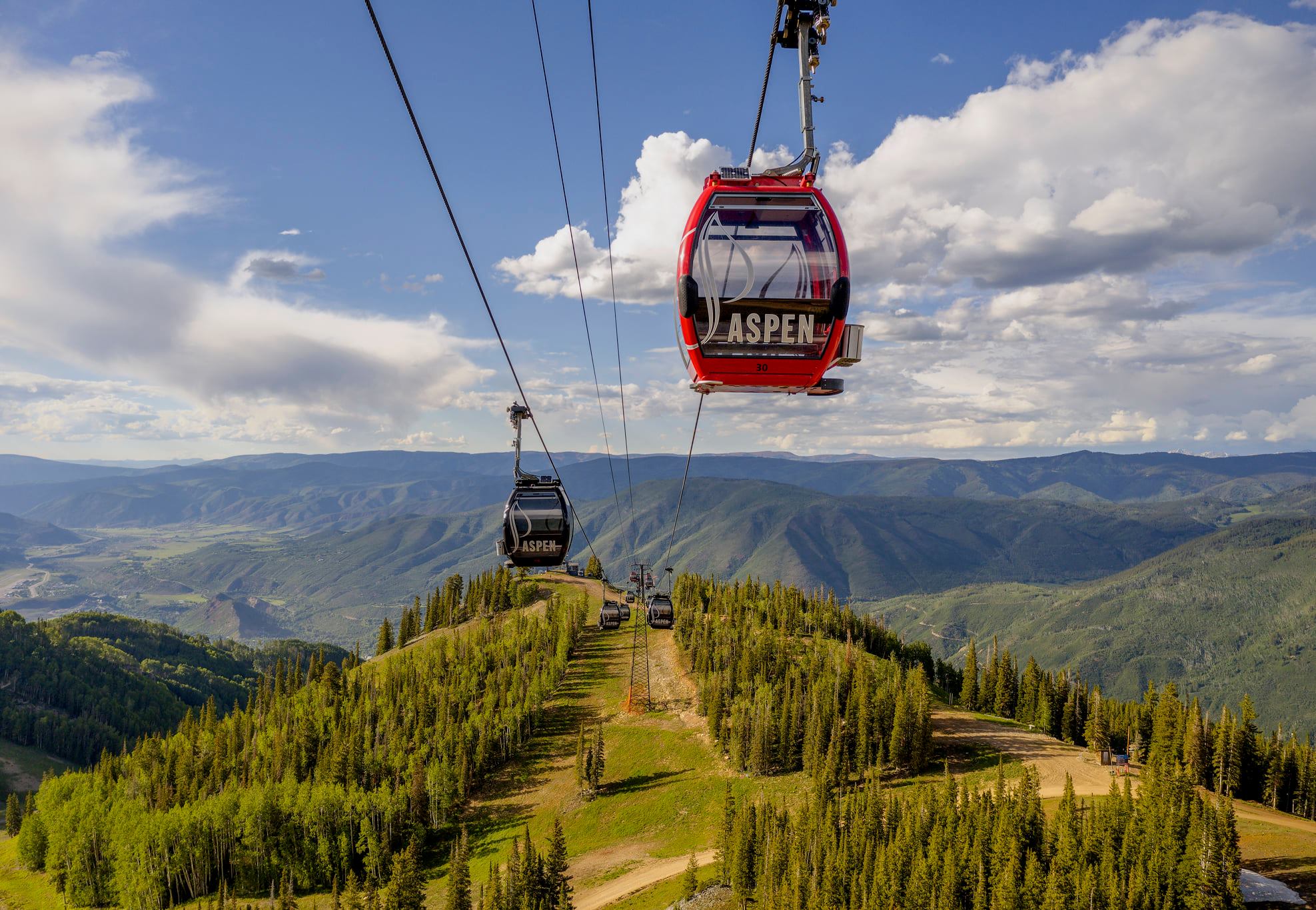 Red gondola car high over green forests