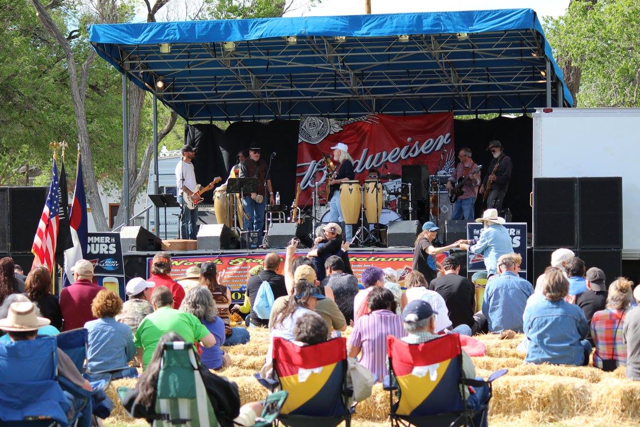 Crowd of people sitting on chairs and hay bales in front of a small stage with musical performers in Alamosa for the Summerfest on the Rio