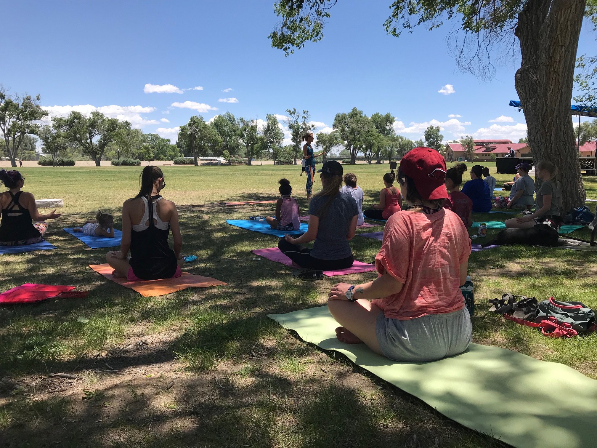 People sitting on a shaded lawn on yoga mats for the weekly Weekends on the Rio community activities in Alamosa